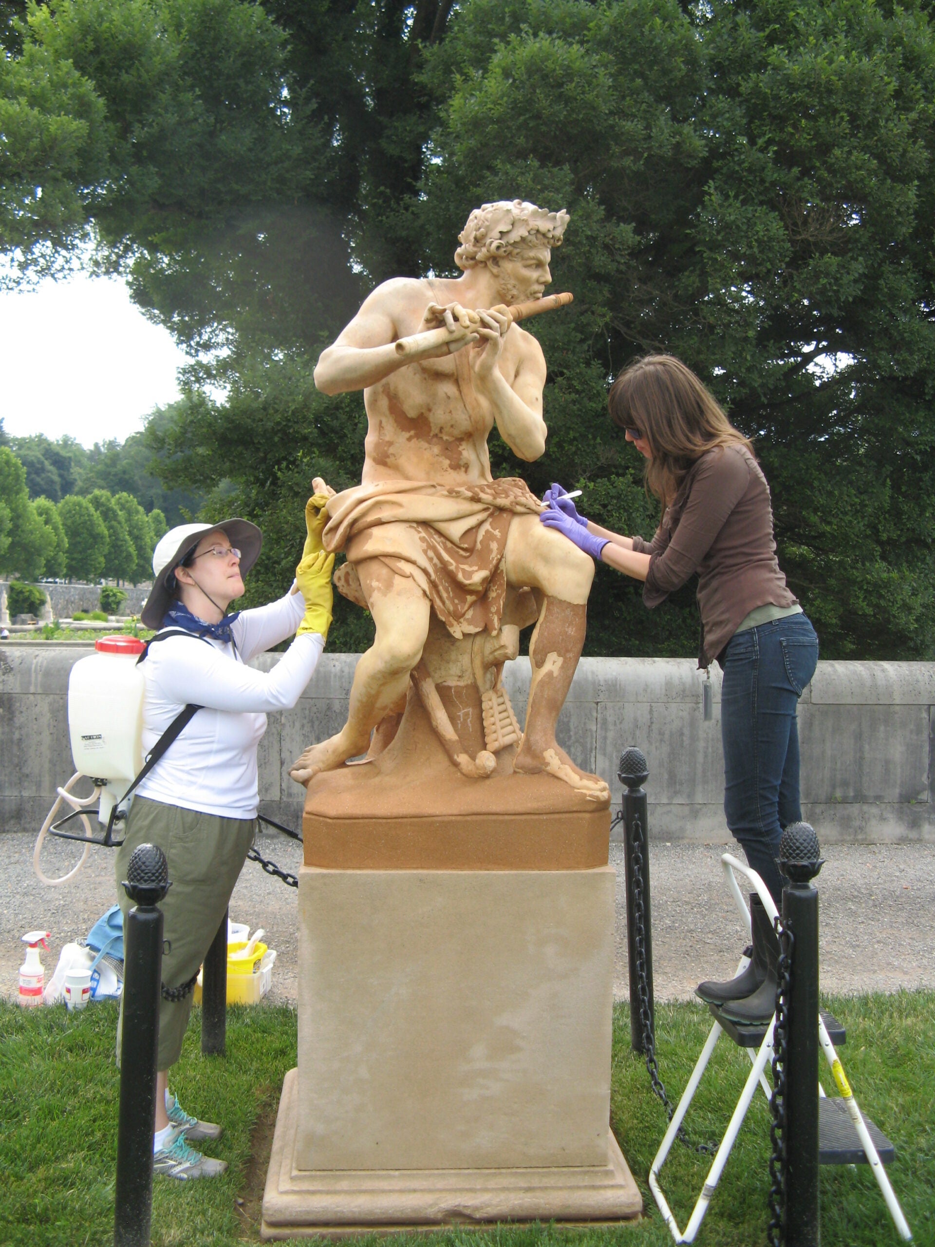 Two women clean an outdoor sculpture of Pan at Biltmore Estate.