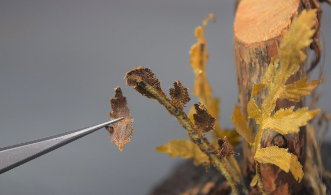 Using tweezers to put original silk botanical leaves back on the base of a taxidermied bird.